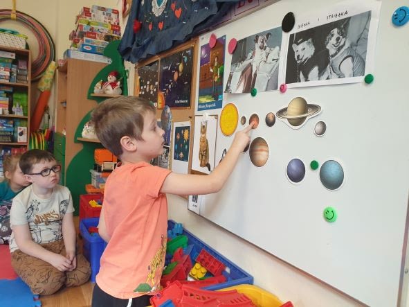 Chłopiec stoi przy tablicy. Wskazuje ilustrację planety.