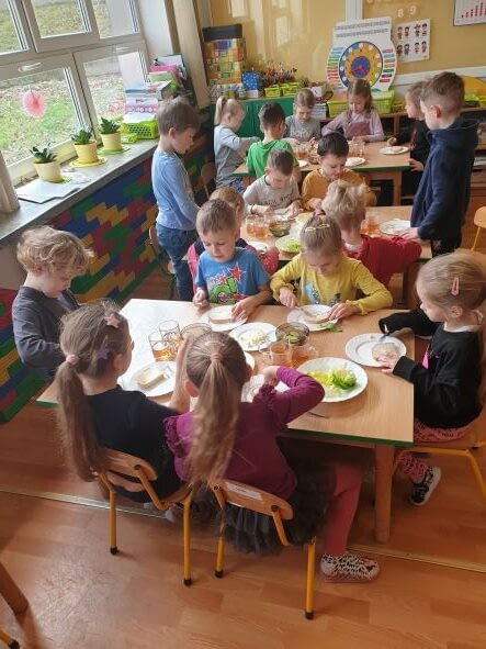 Dzieci siedzą przy stolikach, przygotowują zdrowe drugie śniadanie.