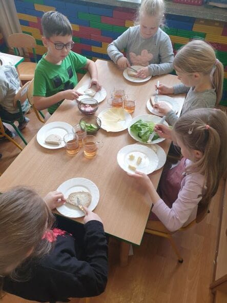 Grupa dzieci siedzi przy stoliku, samodzielnie przyrządza drugie śniadanie.